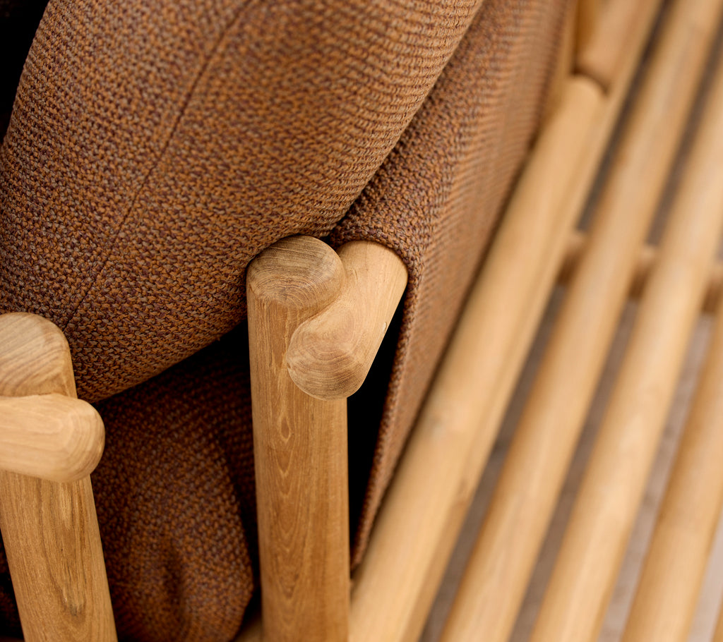 Teak Lounge-Stuhl mit weichen Kissen und stylischen Holzstäben, die die Armlehne und die Basisstruktur bilden.