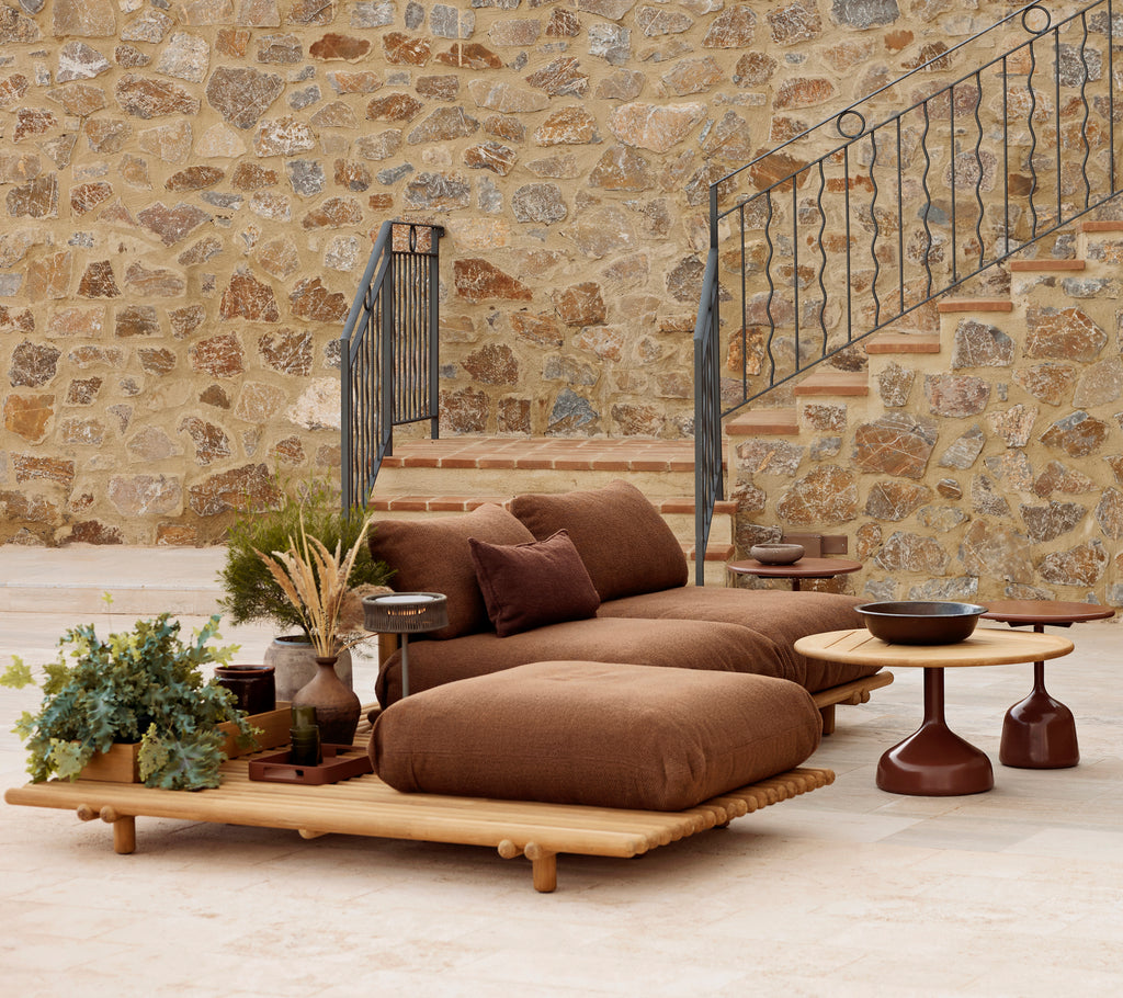 Teak lounge with plush cushions and a Glaze coffee table, complemented by decorative plants and a textured stone backdrop.