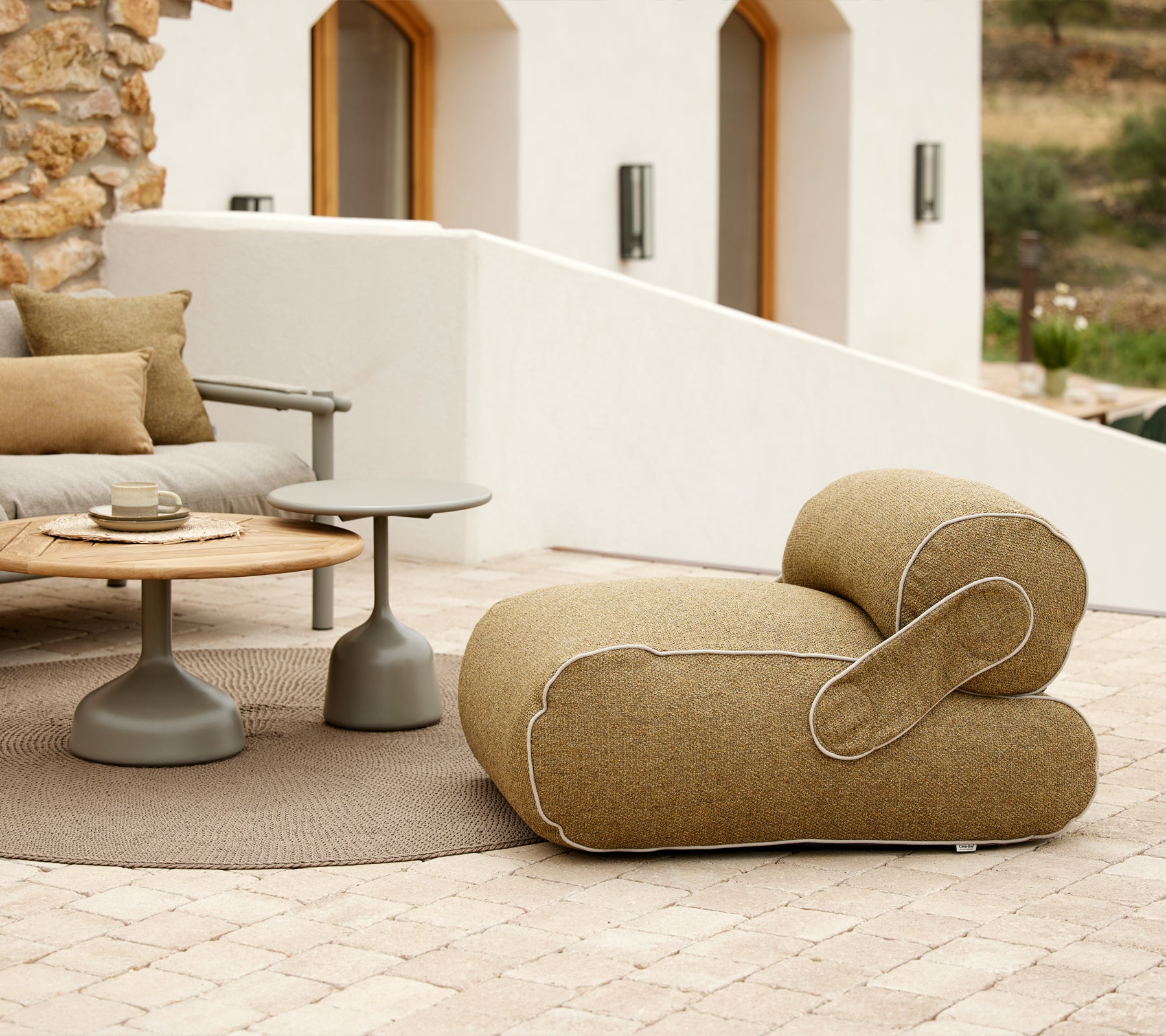Stylischer Loungesessel mit einzigartiger Form, begleitet von einem runden Tisch und dekorativen Kissen, in einer ruhigen Umgebung.