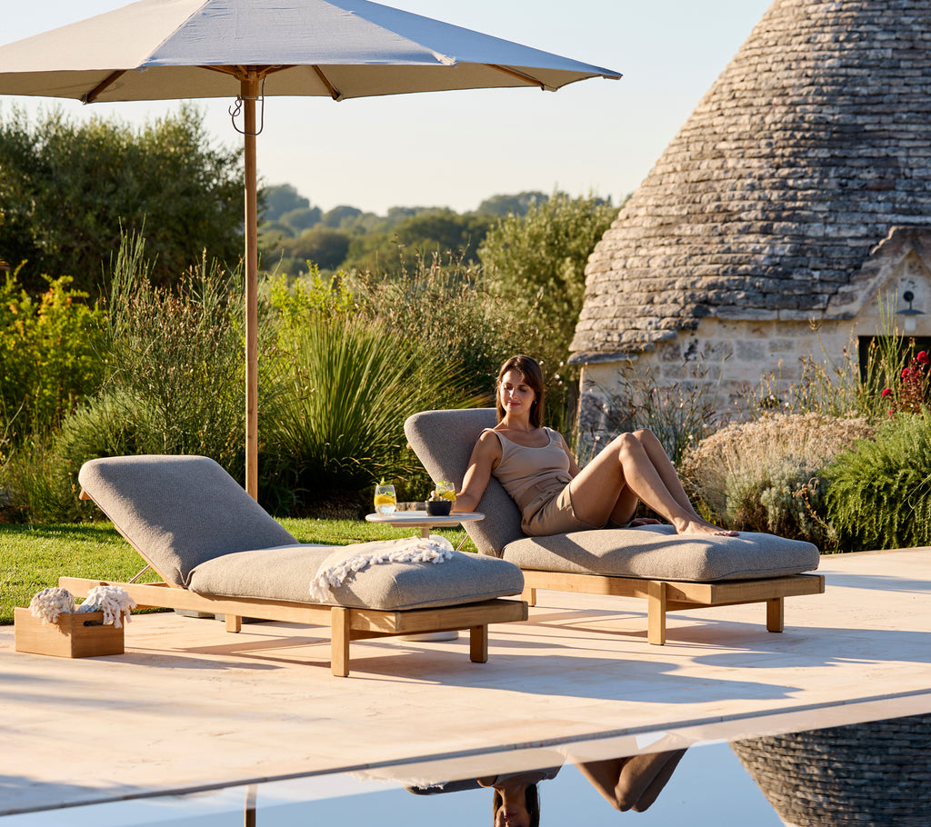 Zwei Liegen mit beigen Kissen unter einem Sonnenschirm in einer ruhigen Außeneinstellung.