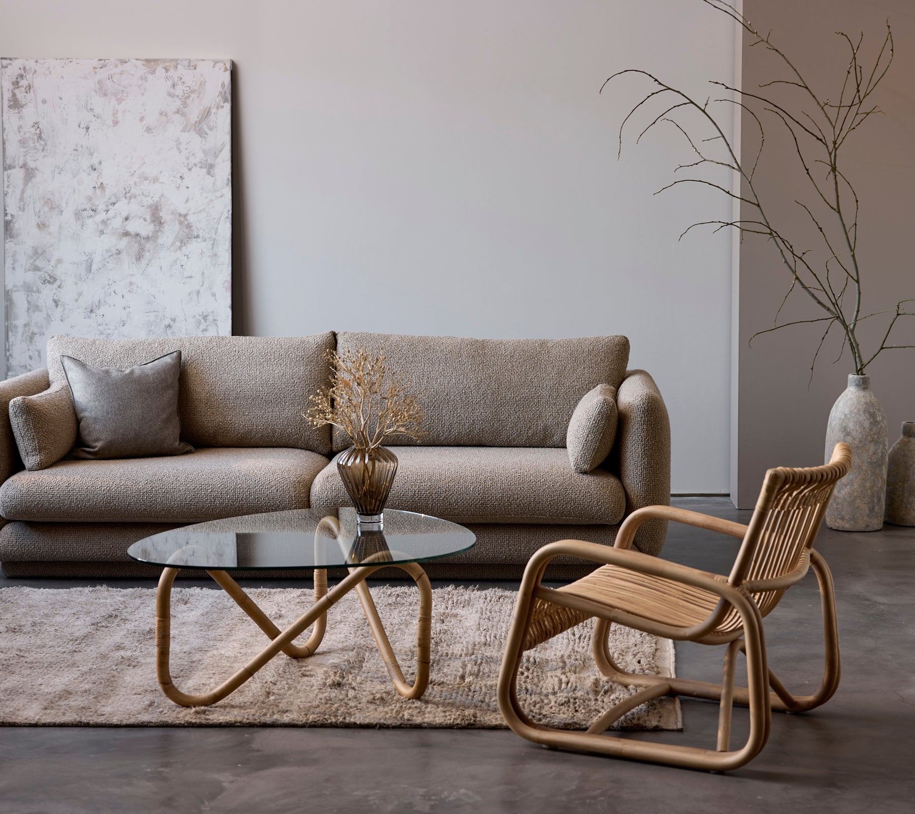 Zeitgenössische Lounge-Einrichtung mit einem beigen Sofa, einem Glastisch und einem geflochtenen Stuhl.