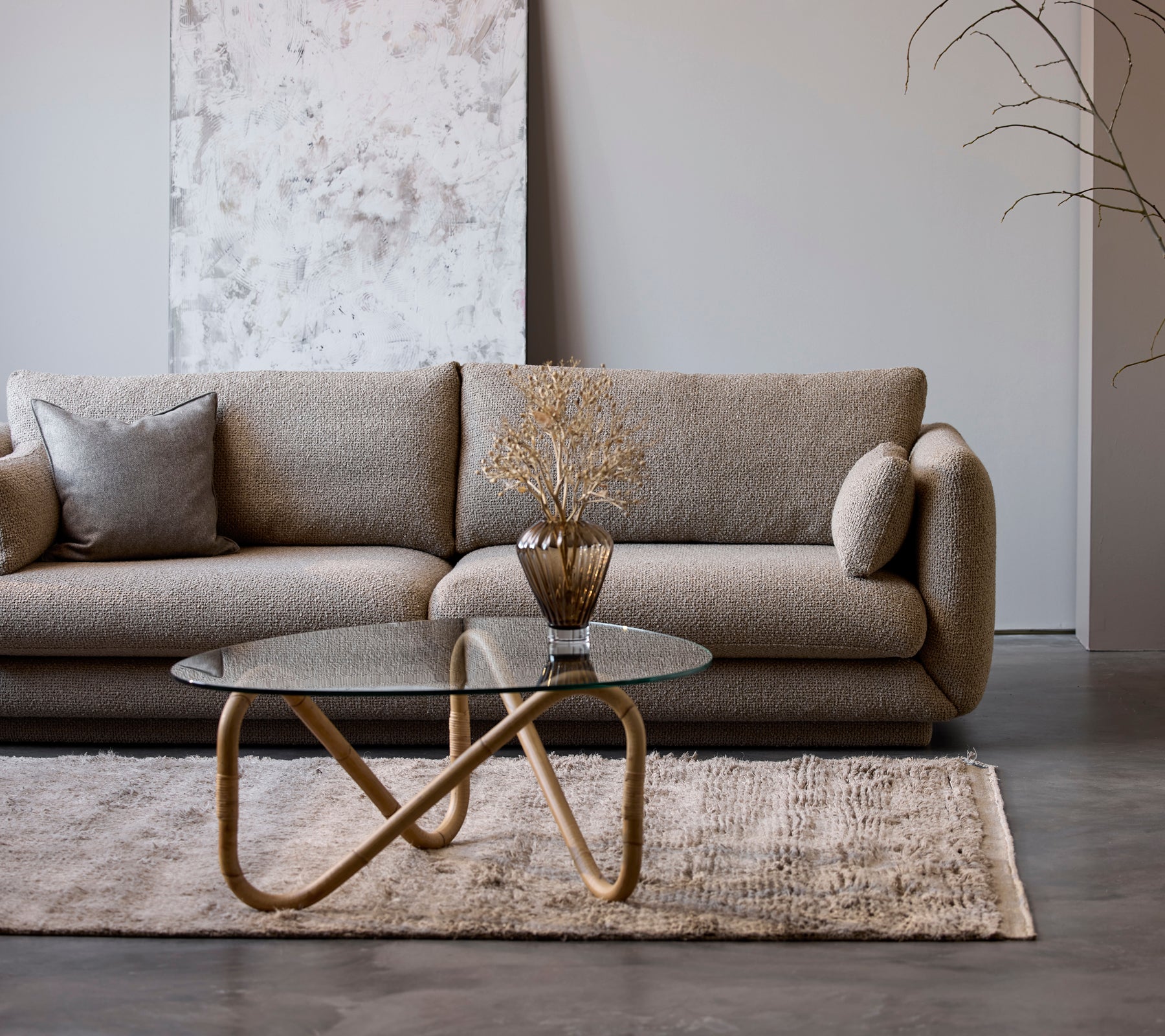 Ein modernes beiges Sofa mit einem Glastisch und einer dekorativen Vase in einer minimalistischen Lounge-Umgebung.