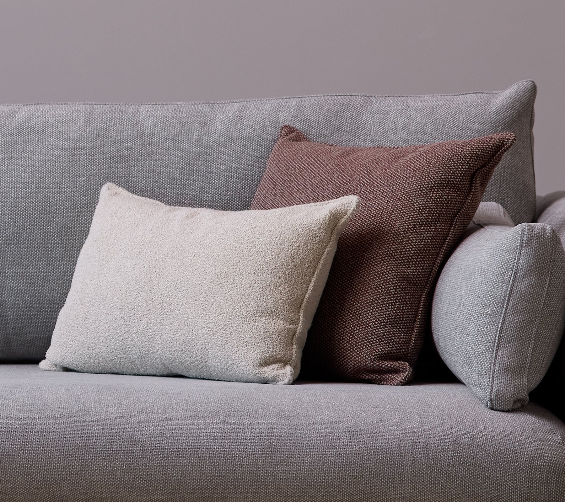 Ein weißes Scent-Kissenscatter und ein Wove dunkelbordeaux Kissen sind auf einem grauen Sofa platziert.