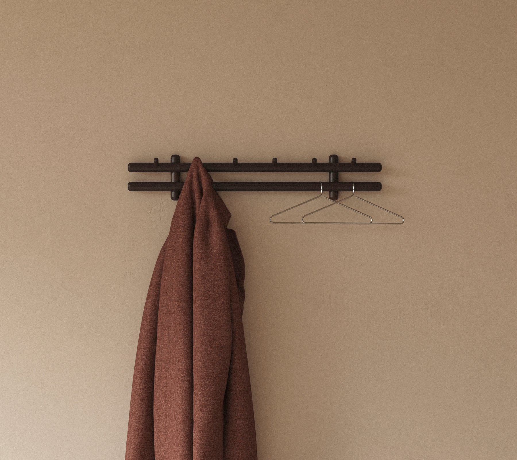 Ein brauner Mantel hängt an einem minimalistischen Wandregal mit Haken, ergänzt durch einen einfachen Drahtkleiderbügel vor einem neutralen Hintergrund.