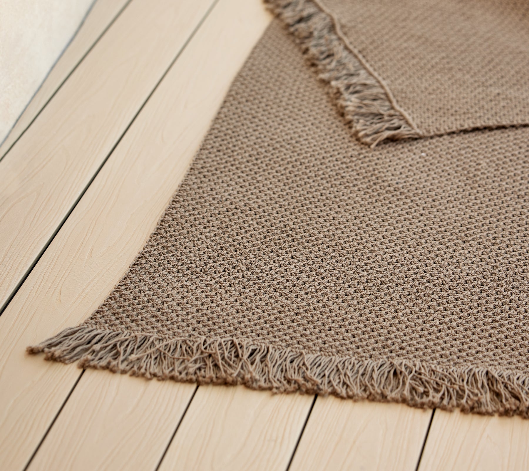 Ein strukturierten Strickteppich mit Fransen, der eine warme, neutrale Farbe zeigt und die gemütliche Ästhetik verstärkt.