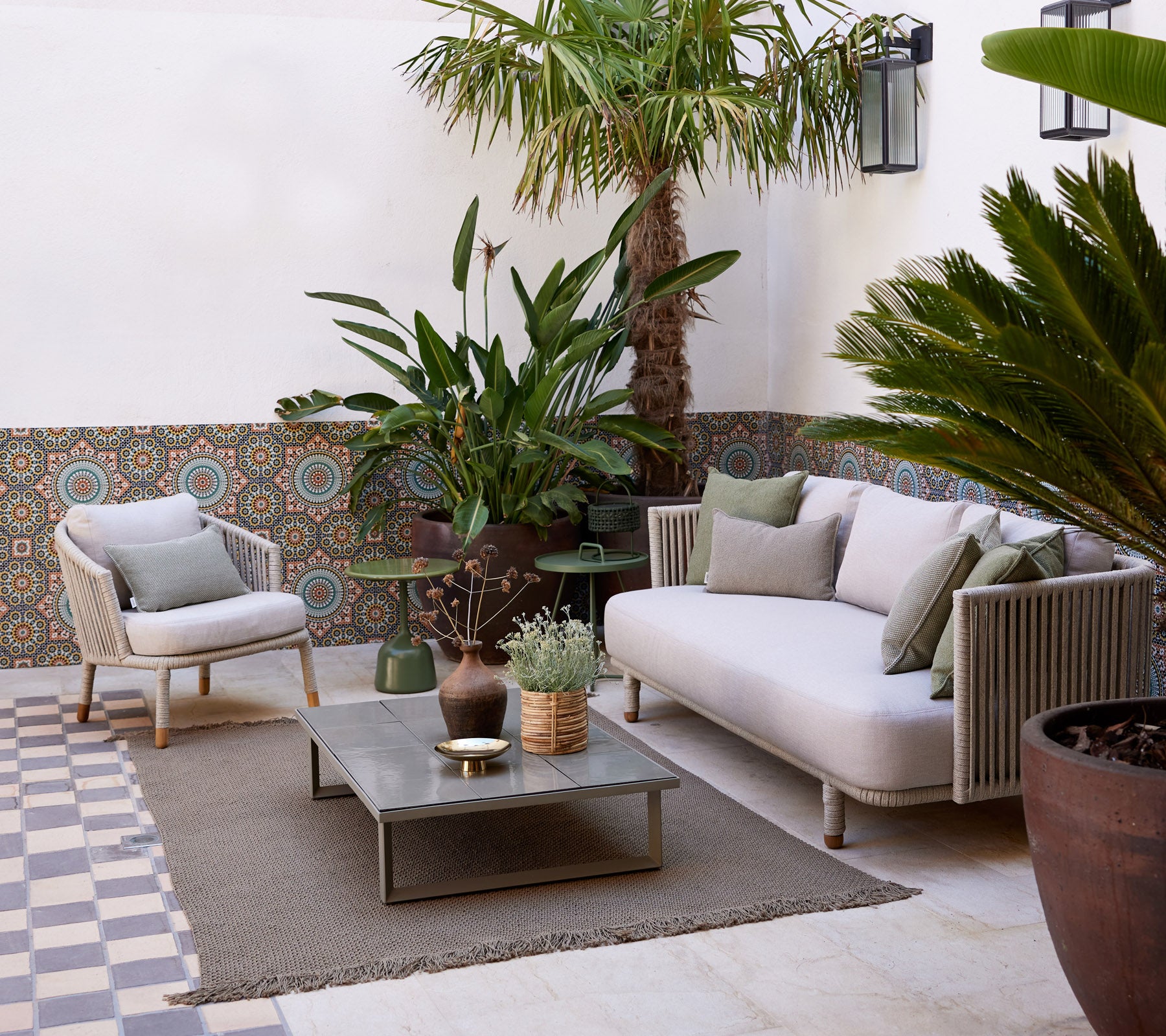 Gemütlicher Lounge-Bereich mit einem hellen Sofa, Topfpflanzen, dekorativem Tisch und strukturiertem Boden, der eine ruhige Atmosphäre schafft.