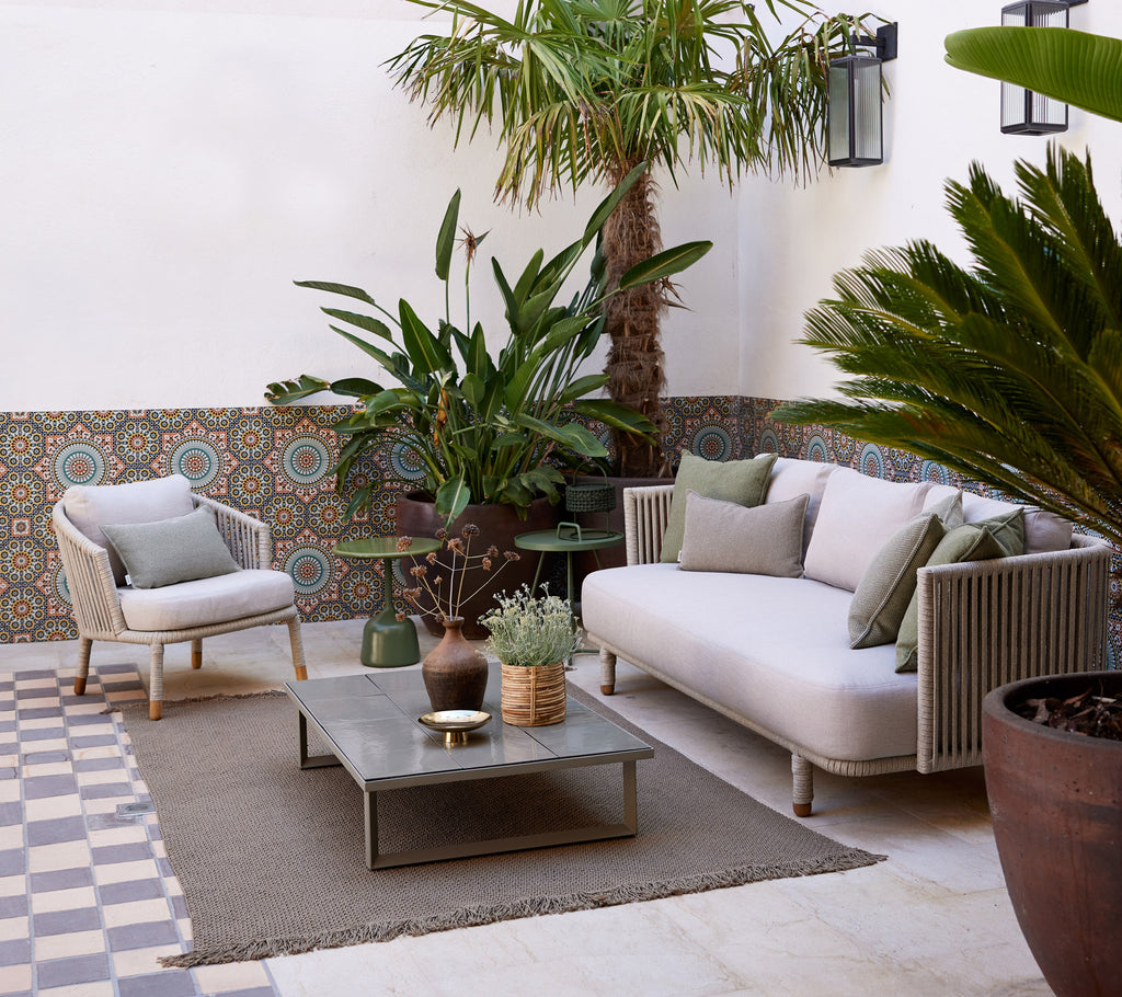 Gemütlicher Lounge-Bereich mit einem hellen Sofa, Topfpflanzen, dekorativem Tisch und strukturiertem Boden, der eine ruhige Atmosphäre schafft.