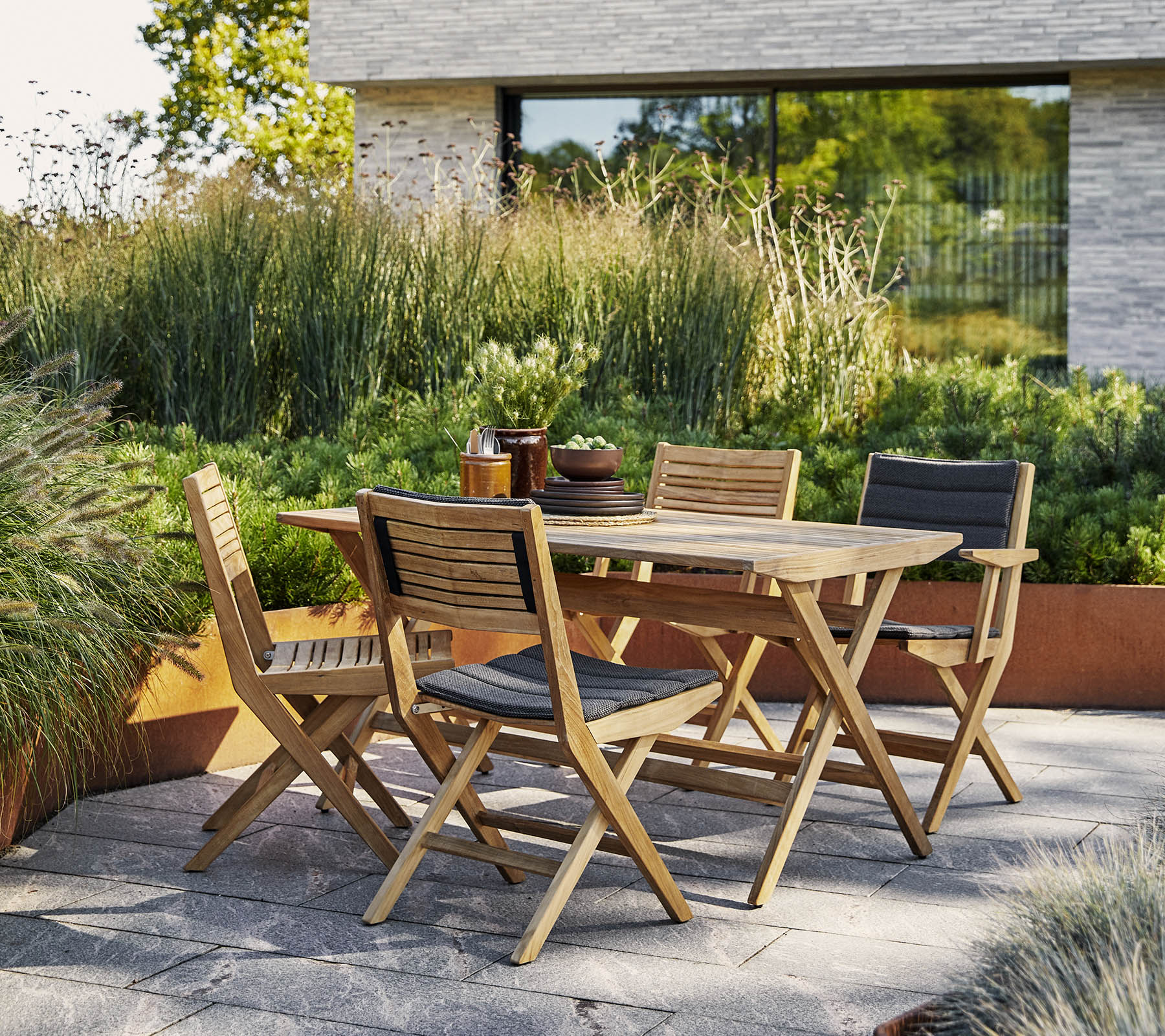 Stylischer Holztisch mit passenden Stühlen, umgeben von üppigem Grün und einer modernen architektonischen Kulisse. Perfekt für Outdoor-Veranstaltungen.